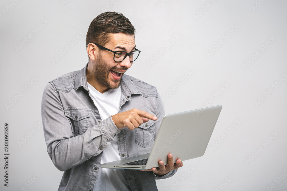 Confident young handsome man in shirt holding laptop and smiling while standing against white background