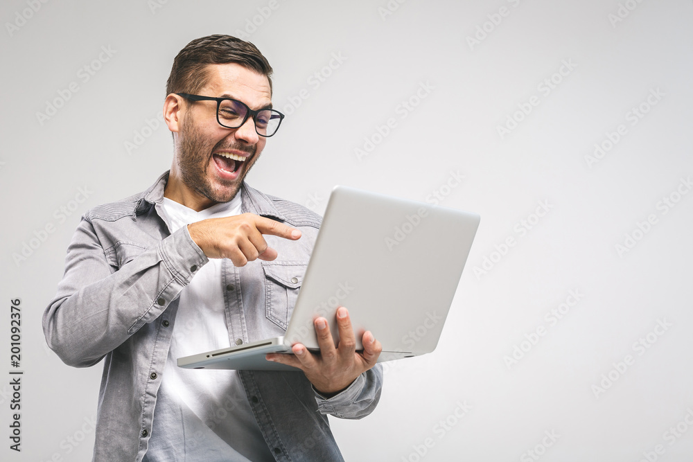 Funny young handsome man in shirt holding laptop and smiling while standing against white background. Have fun. Funny young handsome man in shirt holding laptop and smiling while standing against white background. Have fun.