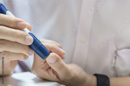 Close up of man hands using lancet on finger to check blood sugar level by Glucose meter using as Medicine, diabetes, glycemia, health care and people concept.