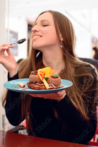 Obraz na płótnie Young woman eats sweet desert. Ice-cream with orange slices on brussel waffle on the plate. Lady tastes delicious meal, has a bite a beautiful cake. Person holding a plate w salonie