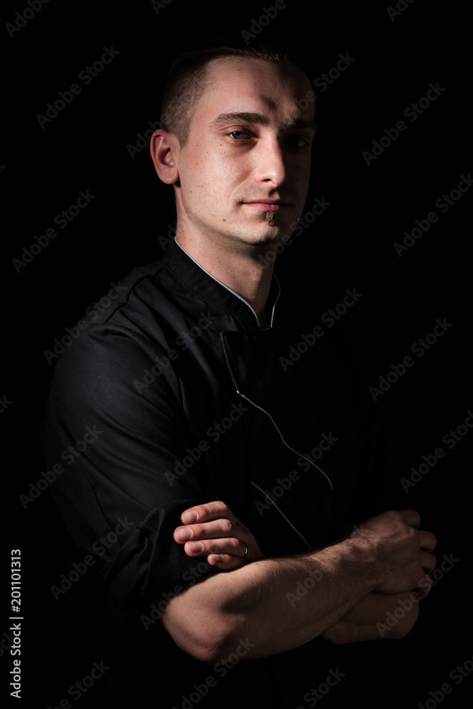 portrait of a young chef in uniform on a black background.