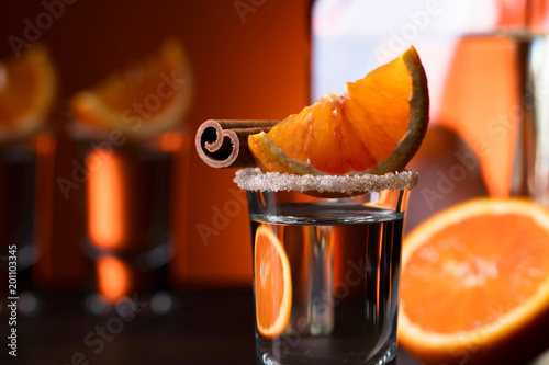 Glasses of tequila with orange and cinnamon sticks on a wooden table.