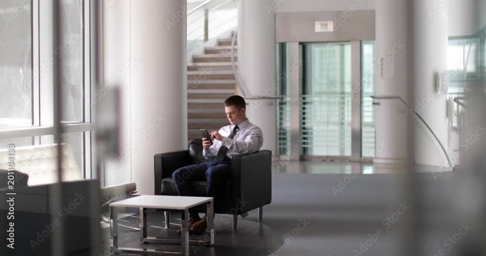 Businessman waiting in office reception using smartphone Businessman waiting in office reception using smartphone