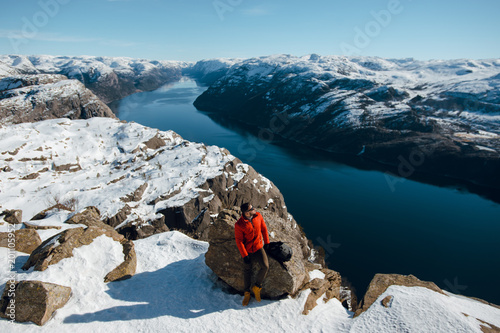 A young man sitting on a Pulpit Rock and admiring the beautiful mountain panorama. Lysefjord, Preikestolen, Norway. View from above