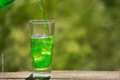 in a tall glass of ice poured a green carbonated drink, against a background of greenery, a concept