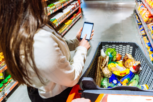 woman hold phone with white screen while make grocery shopping