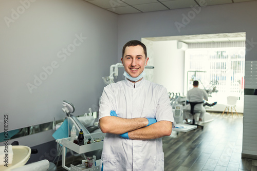 Male dentist standing with his hands crossed over medical office background. Healthcare  profession  stomatology and medicine concept