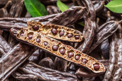 Carob pods and carob beans on the wooden table.