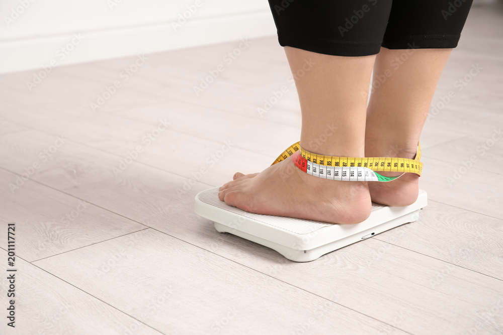 Overweight woman using scales indoors