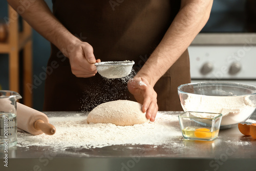 Man sprinkling flour over dough on table in kitchen