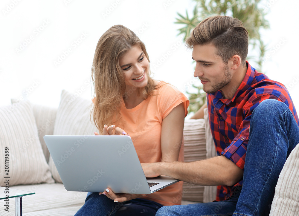 young couple is using a laptop and smiling while sitting on sofa at home