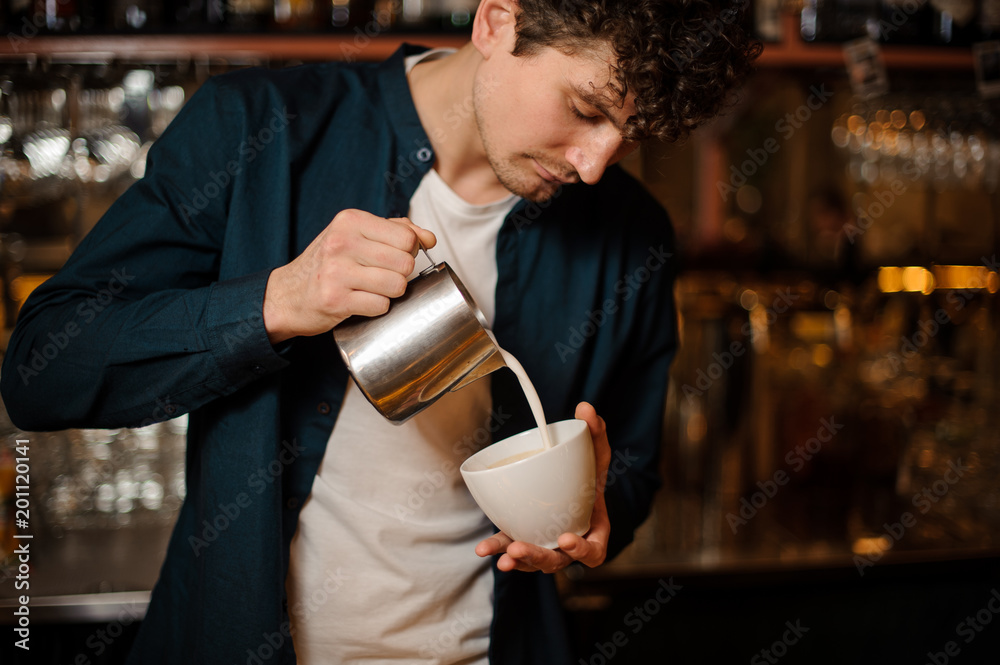Barman pouring some milk from pitcher into a cup