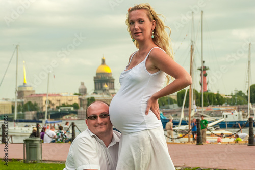 A pair of husband and wife have a rest in the Park. The man squatted down, hugged his wife, and leaned his ear against her stomach, trying to hear the sound of the baby in her stomach.