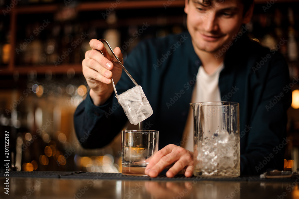 Bartender putting a big ice cube into an empty glass