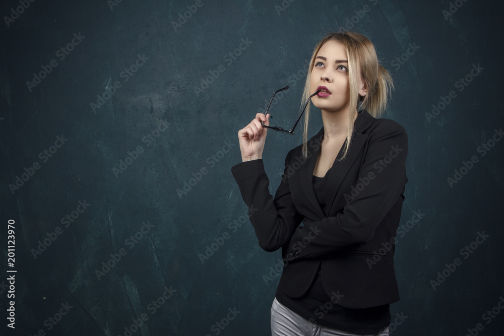 Portrait of a beautiful woman in glasses in a black suit against a blue textural wall with space for text. Portrait of a beautiful woman in glasses in a black suit against a blue textural wall with space for text.