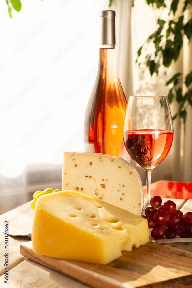 Dutch hard cheese Maasdam or Emmentaler, cheese with holes and white hard goat cheese with coriander served with rose wine Dutch hard cheese Maasdam or Emmentaler, cheese with holes and white hard goat cheese with coriander served with rose wine