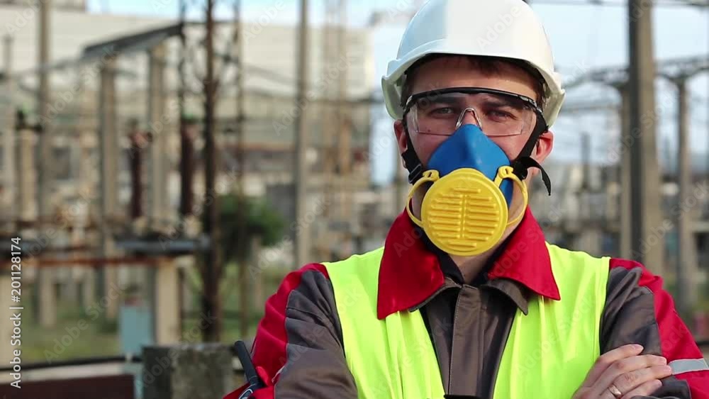 Worker in respirator on electric power station looks at the camera. Power engineering specialist in gas mask, goggles and hard hat at heat power plant Worker in respirator on electric power station looks at the camera. Power engineering specialist in gas mask, goggles and hard hat at heat power plant
