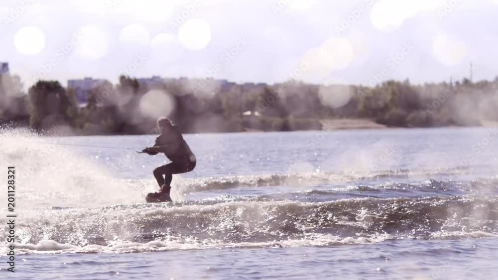 Man making extreme jump on wakeboarding in slow motion. Man doing stunt in water splashes. Guy riding wakeboard on wide river. Extreme water sports Man making extreme jump on wakeboarding in slow motion. Man doing stunt in water splashes. Guy riding wakeboard on wide river. Extreme water sports