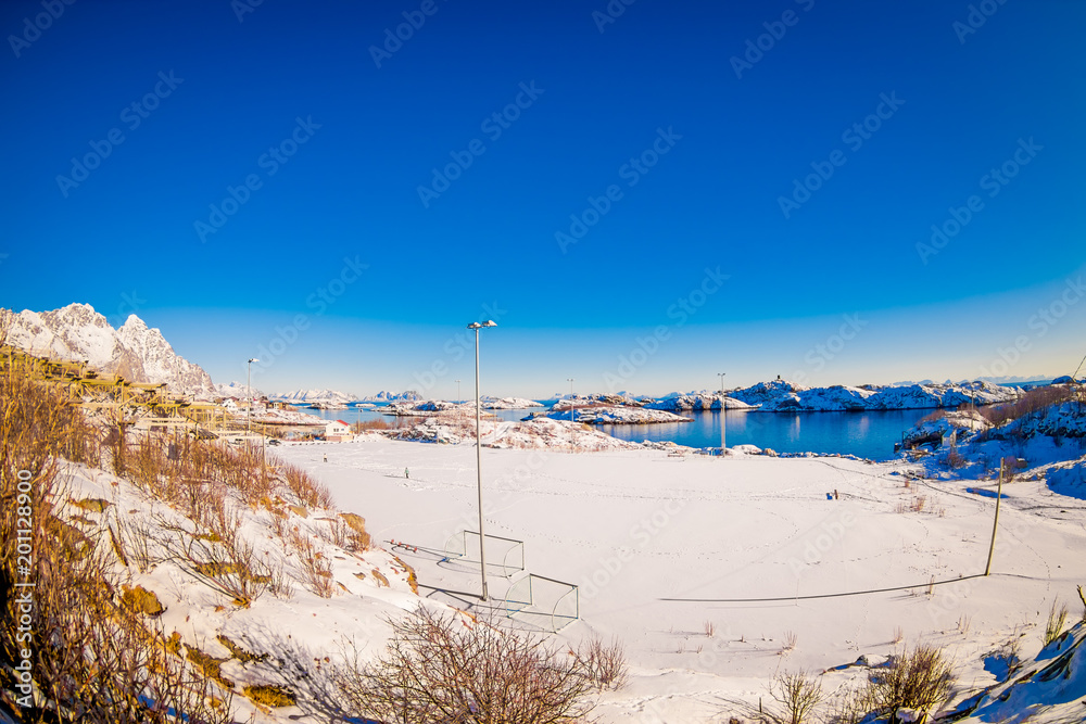 Outdoor view of soccer or hockey field covered with snow i a gorgeus sunny day with blue lake in snowy winter in the Arctic Circle