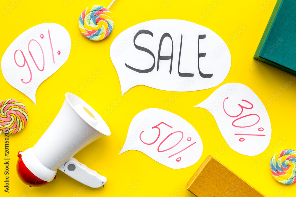 Sale concept with megaphone. Declare the sale. Electronic megaphone near word sale in cloud, gift boxes and sweets on yellow background top view
