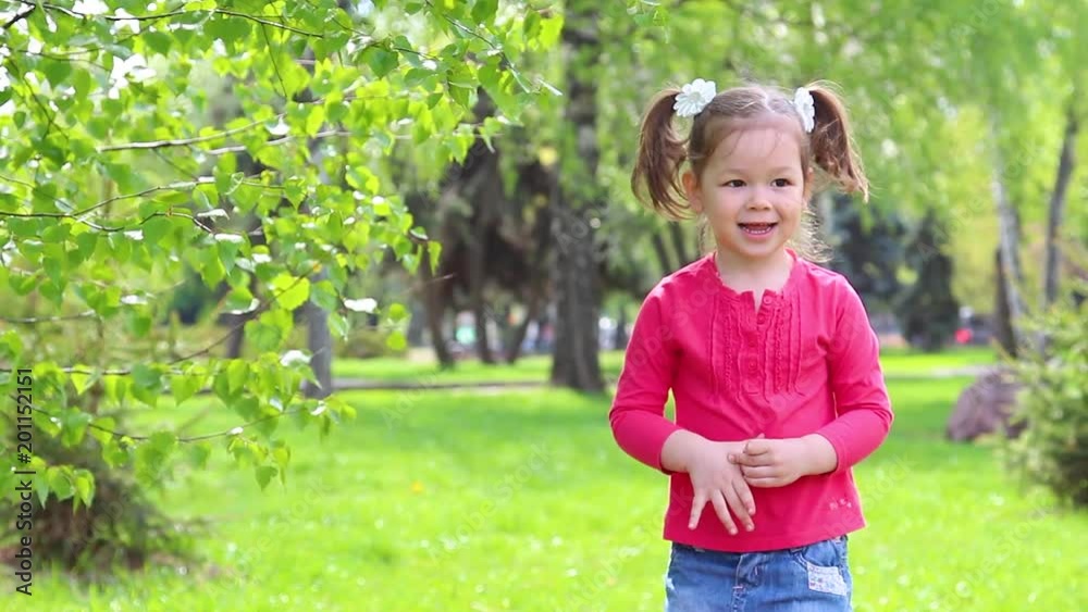 Cute little funny girl playing outdoors happily. Child jumping on green grass lawn in park. Cute little funny girl playing outdoors happily. Child jumping on green grass lawn in park.