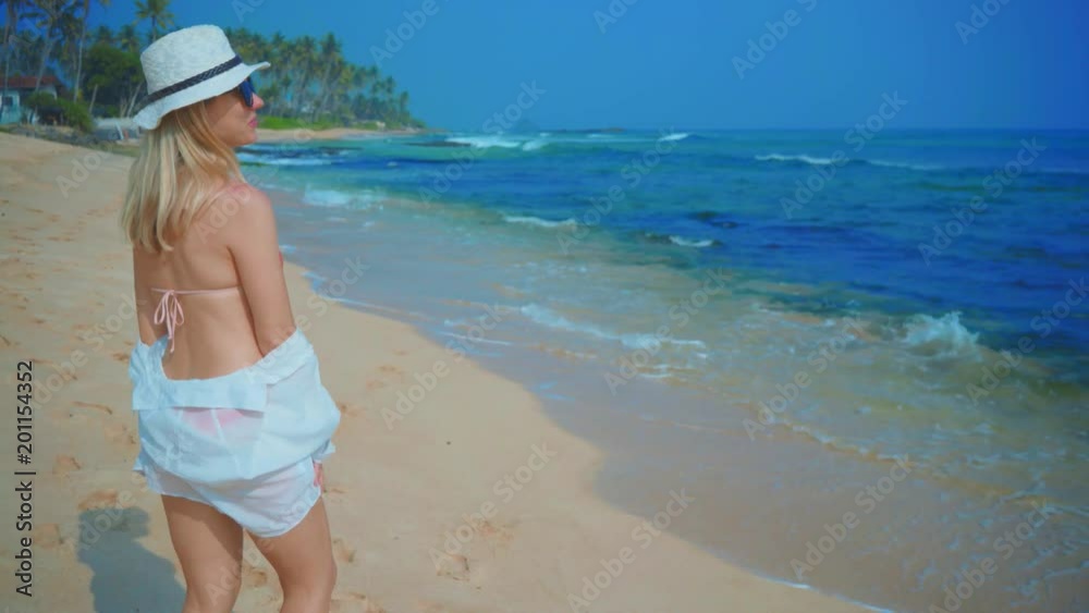 Woman walking on the ocean beach under blue sky in sunny day. Seascape view with palms. Woman walking on the ocean beach under blue sky in sunny day. Seascape view with palms.