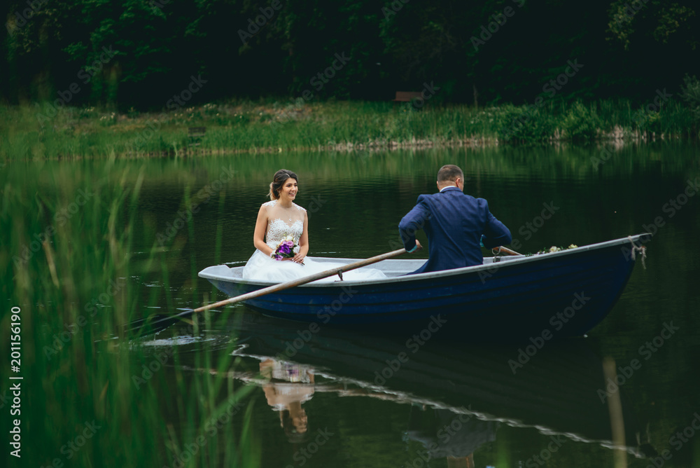 beautiful young wedding couple, blonde bride with flower and her groom just married on small boat at pond beautiful young wedding couple, blonde bride with flower and her groom just married on small boat at pond