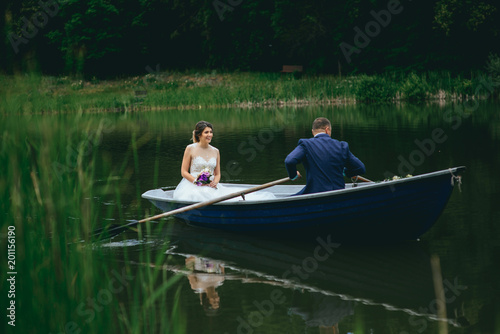beautiful young wedding couple, blonde bride with flower and her groom just married on small boat at pond