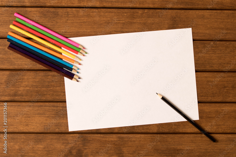 Blank sheet of paper with a set of multicolored pencils on wooden background .Top view. Concept Blank sheet of paper with a set of multicolored pencils on wooden background .Top view. Concept