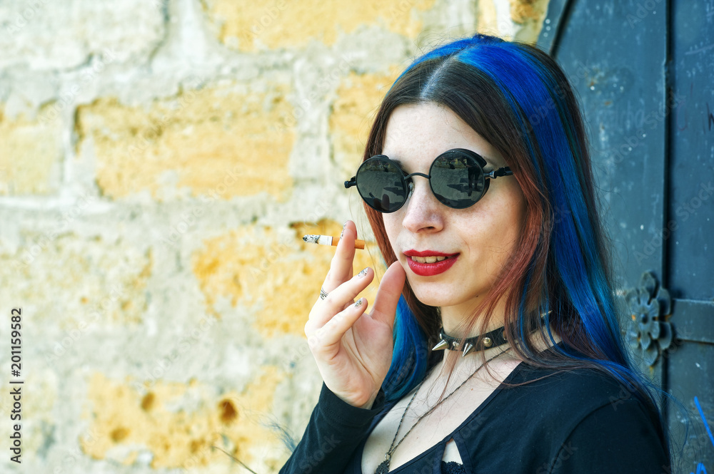 Young girl with blue hair with a cigarette in her hands on the street. Subculture of youth Young girl with blue hair with a cigarette in her hands on the street. Subculture of youth