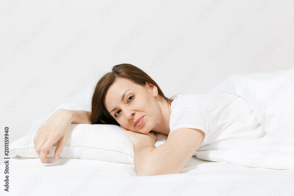 Calm young brunette woman lying in bed with white sheet, pillow, blanket on white background. Smiling beauty female spending time in room. Rest, relax, good mood concept. Copy space for advertisement. Calm young brunette woman lying in bed with white sheet, pillow, blanket on white background. Smiling beauty female spending time in room. Rest, relax, good mood concept. Copy space for advertisement.
