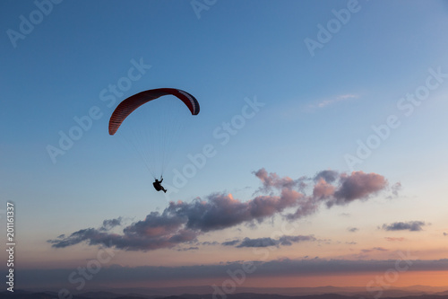 Beautiful shot of a paraglider silhouette flying over Monte Cucco (Umbria, Italy) with sunset on the background, with beautiful colors and dark tones