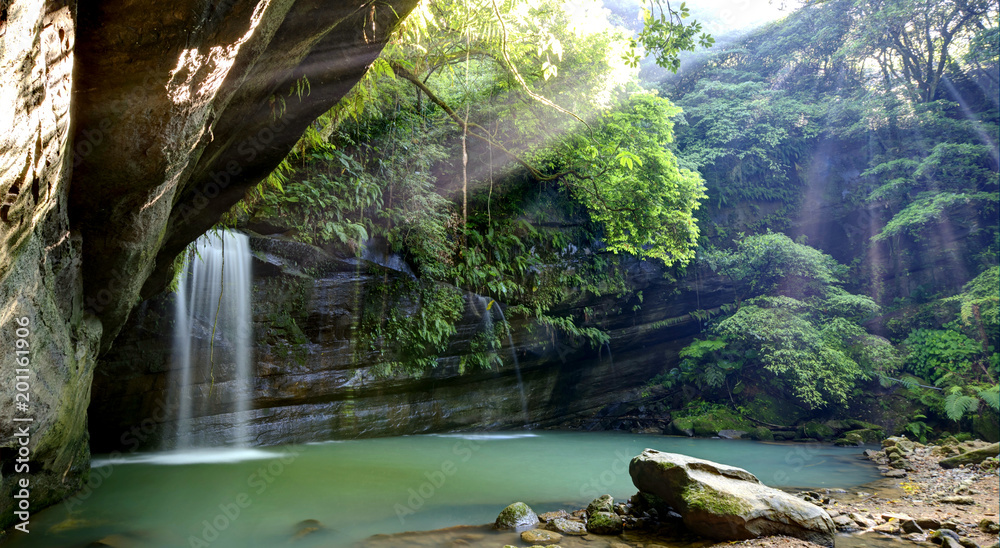 Fototapeta premium A cool refreshing waterfall tumbling down a rocky cliff into an emerald pond hidden in a mysterious forest of lush greenery ~ Scenic view of a beautiful waterfall & intriguing river potholes in Taiwan