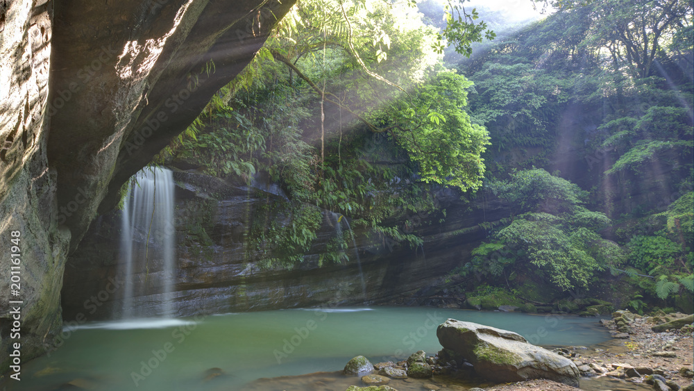 Fototapeta premium A cool refreshing waterfall tumbling down a rocky cliff into an emerald pond hidden in a mysterious forest of lush greenery ~ Scenic view of a beautiful waterfall & intriguing river potholes in Taiwan