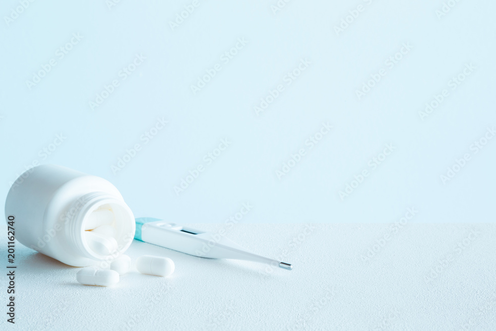 White bottle with pills and digital thermometer on blue background. Fever and healthcare concept. Mock up for special offers as advertising or other ideas. Copy space. Empty place for text or logo. White bottle with pills and digital thermometer on blue background. Fever and healthcare concept. Mock up for special offers as advertising or other ideas. Copy space. Empty place for text or logo.