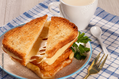 Toasted slices of bread with cheese and green parsley on white plate, fork, cup of coffee and spoon on napkin