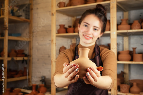 a young and cheerful woman holding a vase of clay. The potter works in a pottery workshop with clay. the concept of pottery mastery and creativity
