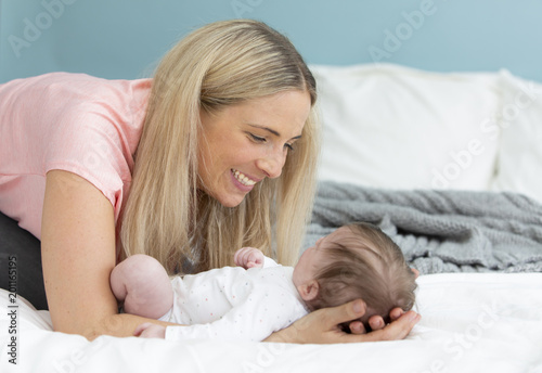 young, beautiful and blond mother with pink shirt is cuddling with her baby in bed