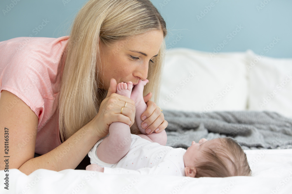 young, beautiful and blond mother with pink shirt is cuddling with her baby in bed young, beautiful and blond mother with pink shirt is cuddling with her baby in bed