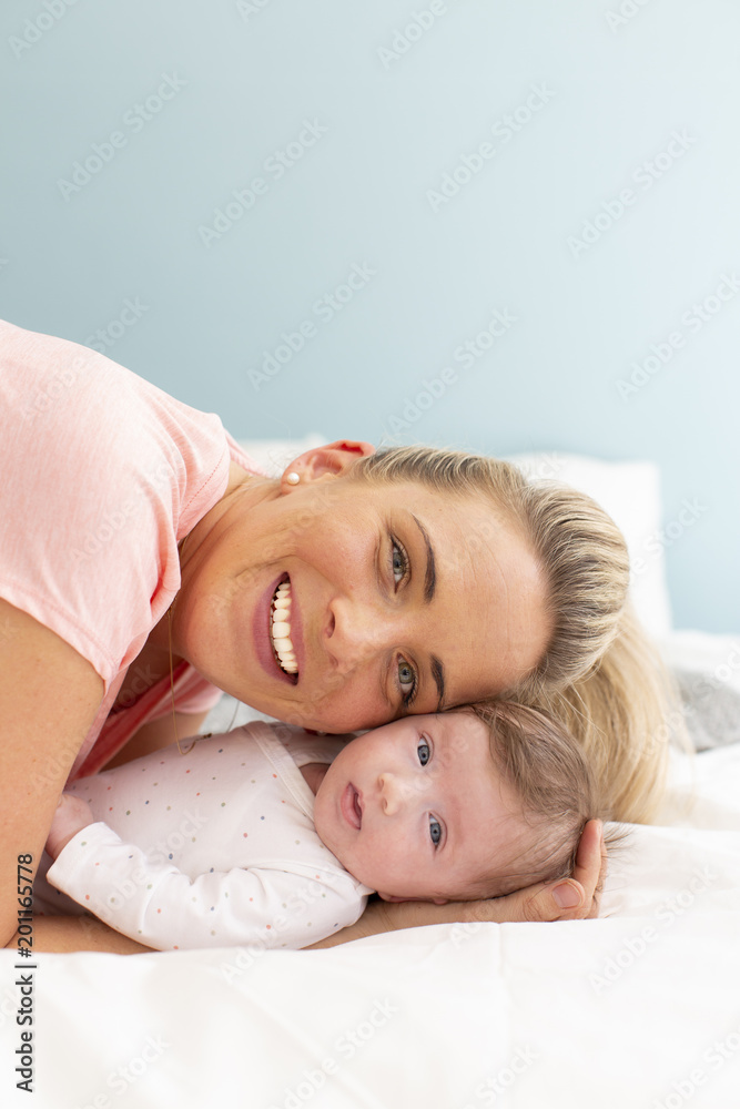 young, beautiful and blond mother with pink shirt is cuddling with her baby in bed young, beautiful and blond mother with pink shirt is cuddling with her baby in bed