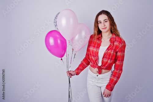 Young girl in red checked shirt and white pants with balloons against white background on studio.