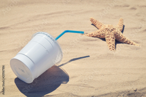 A cup of disposable plastic on the beach. The concept of plastic contamination
