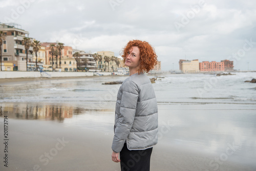 happy young woman in puffer jacket on seashore, Anzio, Italy