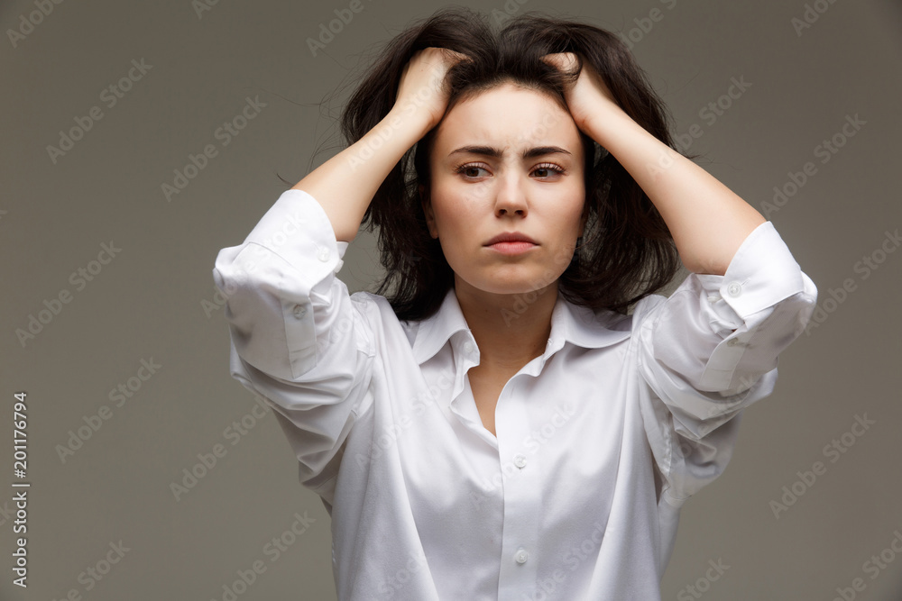 Beautiful girl in a white shirt shows emotions - thoughtfulness. On a light background. Beautiful girl in a white shirt shows emotions - thoughtfulness. On a light background.