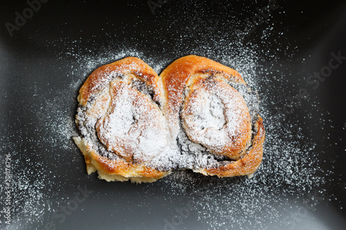 Bun on a black plate with powdered sugar on black background