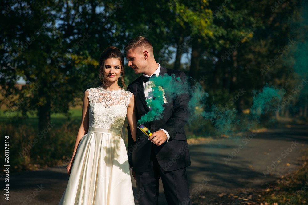Wedding couple hold colored smoke in their hands in the middle of alley