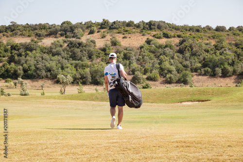 Golfer carrying his bag and clubs across a course. photo