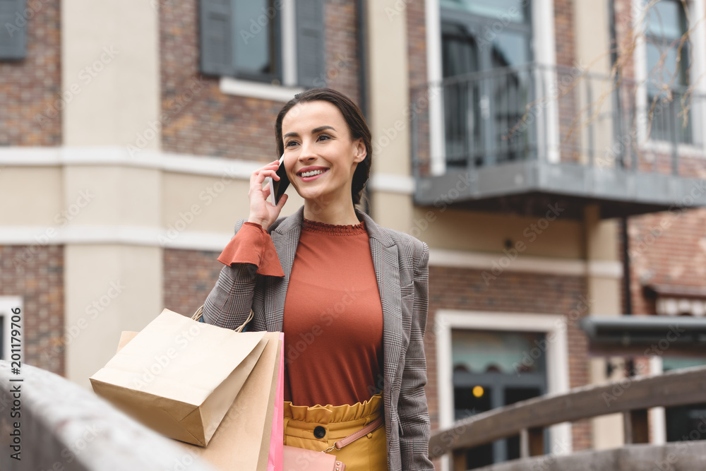 Fototapeta premium smiling woman walking after shopping and talking by smartphone