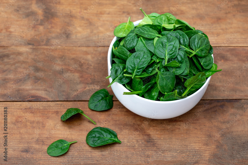 Fresh baby spinach in a bowl on rustic wooden background, top view. Copy space. Fresh baby spinach in a bowl on rustic wooden background, top view. Copy space.