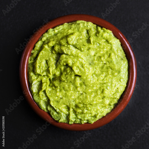 Guacamole spread in clay bowl on a black background. Avocado sauce. Top view with copy space.
